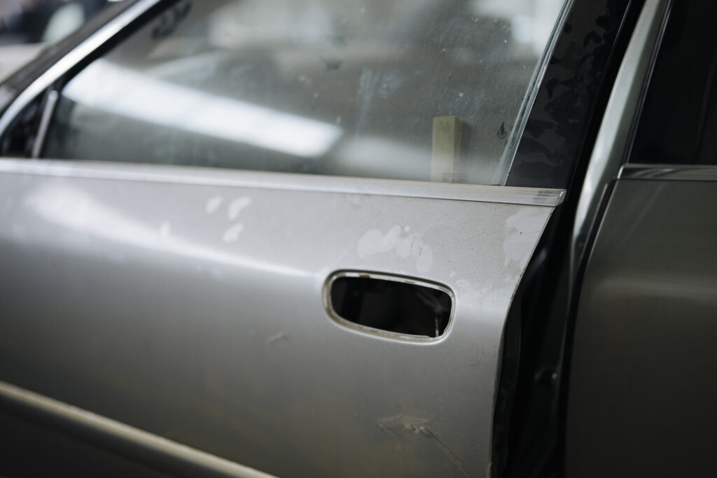 Portiera di un'automobile con una lunga graffiatura sulla vernice e il paraurti segnato