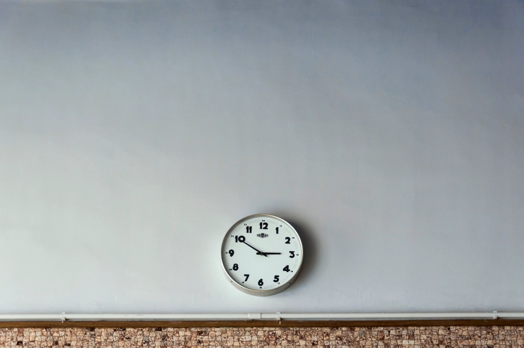 Orologio analogico da parete con lancette nere e quadrante chiaro su una parete spoglia