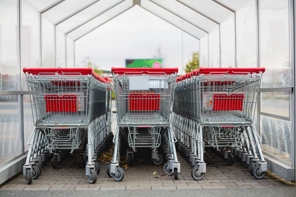 Carrello della spesa fermo in una corsia di supermercato tra scaffali pieni di prodotti