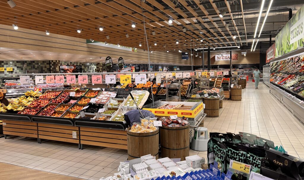 Corsia di un supermercato con banchi di frutta e verdura esposte in cassette