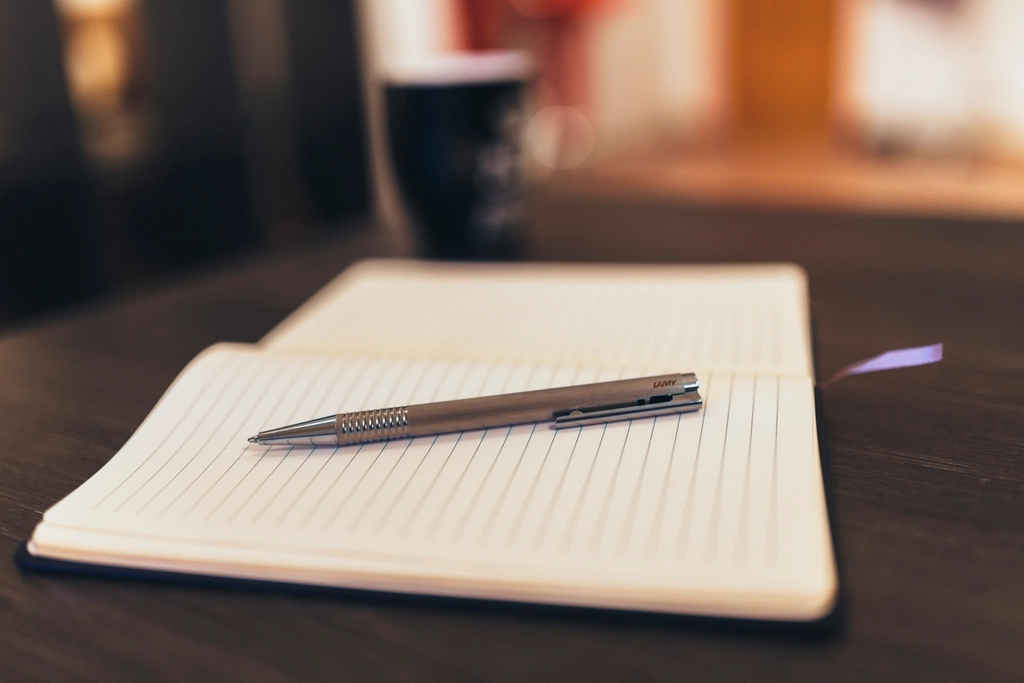 Quaderno aperto con pagine bianche e una penna appoggiata su una scrivania